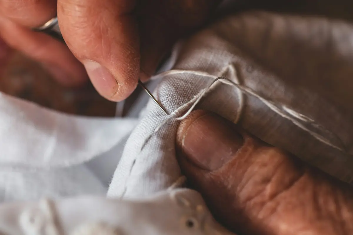 Mãos costurando um tecido branco com agulha e linha