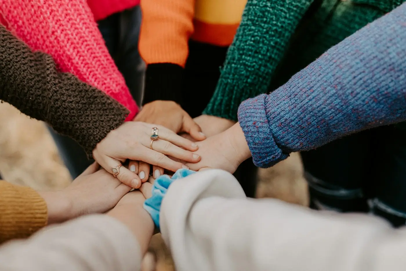 Mãos de várias pessoas unidas no centro, com roupas coloridas